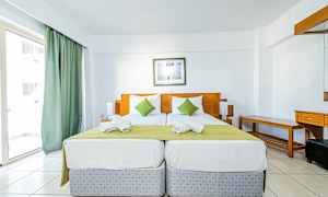 To enkeltsenge med grønt sengetæppe og hvide puder i et hotelværelse med lys indretning. (AI-genereret tekst)