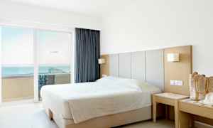 Et hotelværelse med en dobbeltseng tæt på vinduet med udsigt over havet. (AI-genereret tekst)