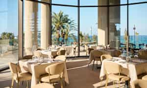 En lys og elegant restaurant med panoramavinduer med udsigt til palmer og hav. (AI-genereret tekst)