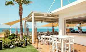 En udendørsrestaurant med borde og stole, udsigt over havet og klar blå himmel. (AI-genereret tekst)