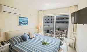 Et hotelværelse med en dobbeltseng, dekoreret i blå nuancer, og en altan med møbler, der vender mod en nærliggende bygning. (AI-genereret tekst)