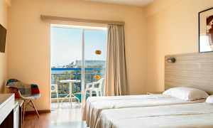 Et hotelværelse med to enkeltsenge, en stol, fjernsyn og en balkon med udsigt. (AI-genereret tekst)