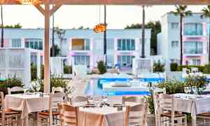 Restaurantborde med hvide duge ved en pool, omgivet af moderne arkitektur. (AI-genereret tekst)