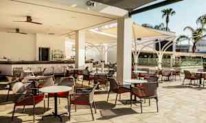 Billede af en udendørsterrasse med borde og stole samt en bar. (AI-genereret tekst)