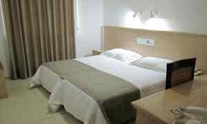 Et hotelværelse med en dobbeltseng, sengelamper og et bord med telefon. (AI-genereret tekst)