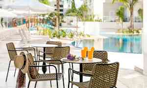 Et bord med kurvestole ved et poolområde, med to glas juice og en solhat på stolen. (AI-genereret tekst)