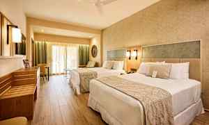 Hotelværelse med to senge, siddeområde og lyse møbler. (AI-genereret tekst)