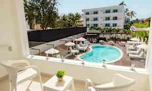 En balkon med to hvide stole og et bord med en grøn plante, med udsigt over en pool og liggestole. (AI-genereret tekst)