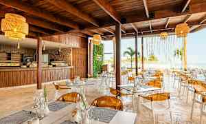 En moderne restaurant med træmøbler, gule lamper og udsigt over havet. (AI-genereret tekst)