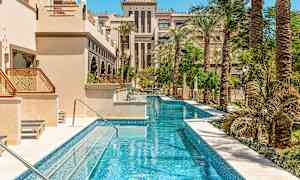 En lang smal pool omgivet af palmer og bygninger med arabisk arkitektur. (AI-genereret tekst)