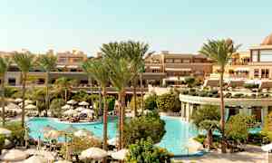 Et hotelområde med en stor pool omgivet af palmer og parasoller. (AI-genereret tekst)