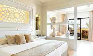 Et lyst og elegant soveværelse med dekorerede vaser på en hylde, en stor seng med puder og adgang til en altan. (AI-genereret tekst)