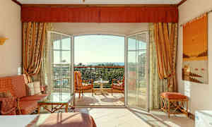 Et hotelværelse med åben altandør, siddepladser og udsigt mod havet. (AI-genereret tekst)