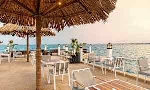 Udendørs serveringsområde med solsikre parasoller nær havet. (AI-genereret tekst)