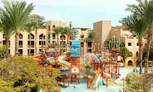 Billede af en vandpark med rutsjebaner og legeinstallationer, omgivet af palmer og hotelbygninger. (AI-genereret tekst)