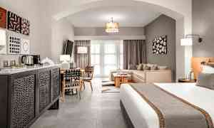 Et hotelværelse med en seng, siddeområde og spisebord samt moderne indretning. (AI-genereret tekst)