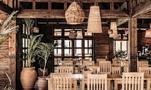 Interiør af en restaurant med trædetaljer, planter og flettede lamper. (AI-genereret tekst)