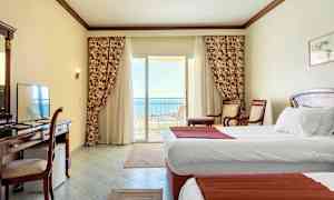 Hotelværelse med hvide vægge, to enkeltsenge og en balkon med udsigt til havet. (AI-genereret tekst)