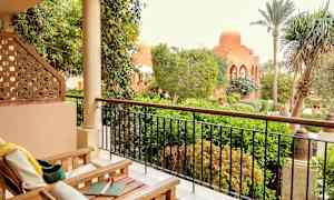 En terrasse med træstole og udsigt over en frodig have og en bygning med kuppel. (AI-genereret tekst)