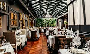 Restaurant med elegante borde, duge og glas. Væggene er dekoreret med kunst, og rummet har glastag. (AI-genereret tekst)