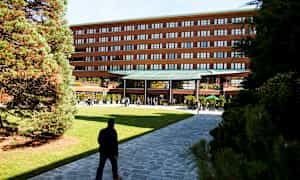 En bygning med en moderne indgang omgivet af grønne områder og gangstier. (AI-genereret tekst)