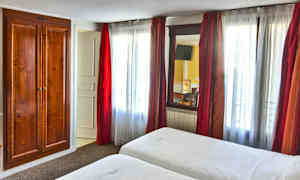 Et hotelværelse med to senge, hvide lagener og et trægarderob ved siden af et vindue med røde gardiner. (AI-genereret tekst)