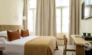 Hotelværelse med en dobbeltseng, puder og et sengetæppe i brune nuancer samt et skrivebord med en kaffemaskine. (AI-genereret tekst)