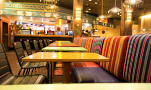 En restaurant med farverige borde og stole samt stribede bænkesæder. (AI-genereret tekst)