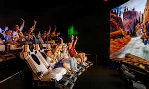 En gruppe personer sidder i en interaktiv simulator med en stor skærm, der viser en naturscene med bjerge og flod. (AI-genereret tekst)