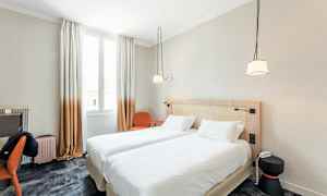 Et hotelværelse med to sammenkoblede enkeltsenge, et skrivebord, en stol og et vindue med lysindfald. (AI-genereret tekst)