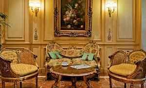 Et elegant indrettet rum med en overdådigt dekoreret sofa, to matchende lænestole og et sofabord foran. Et oliemaleri på væggen over sofaen. (AI-genereret tekst)