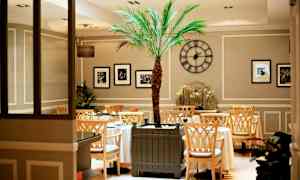 Inde i en elegant café med et centralt placeret palmetræ og dekorative elementer. (AI-genereret tekst)