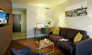 En stue med sofa, lænestol, sofabord med kaffekop og croissant, skrivebord og dekorative detaljer. (AI-genereret tekst)