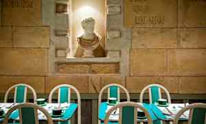 Billedet viser en restaurant med turkise borde og stole samt en hvid skulptur i en niche på væggen. (AI-genereret tekst)