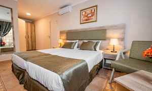 Hotelværelse med to senge, sengetøj og natbord med lampe. (AI-genereret tekst)