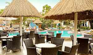 Stole og borde ved en pool med stråtag. (AI-genereret tekst)