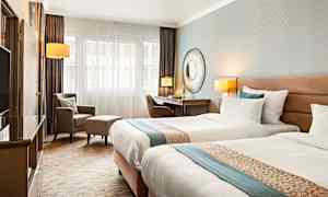 Et hotelværelse med to enkeltsenge, skrivebord, stol og lænestol. (AI-genereret tekst)