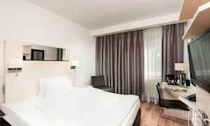 Et hotelværelse med en dobbeltseng, skrivebord og stol samt et stort vindue med gardiner. (AI-genereret tekst)