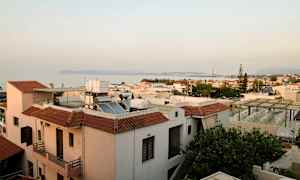 Udsigt over hustage i en kystby med havet og bjerge i baggrunden. (AI-genereret tekst)