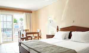 Et hotelværelse med to senge, et træbord og stole samt en balkon med udsigt over poolområdet. (AI-genereret tekst)