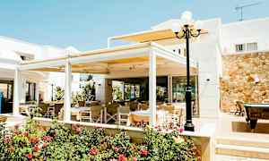 Udendørs serveringsområde med borde og stole ved en bygning, omgivet af blomster og planter. (AI-genereret tekst)