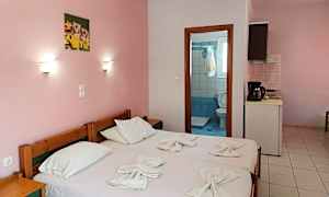 Et enkelt hotelværelse med lyserøde vægge, to enkeltsenge og udsigt ind mod badeværelsesdøren. (AI-genereret tekst)