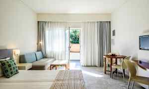 Hotelværelse med redt seng, siddeområde, rundt spisebord og altandør. (AI-genereret tekst)