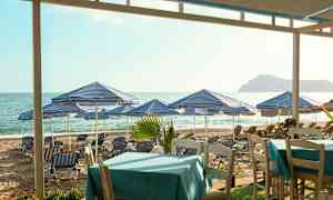 Strand med blå-hvidstribede parasoller og liggestole, borde i forgrunden. (AI-genereret tekst)