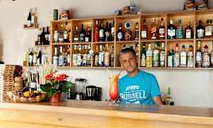 En bar med hylder fyldt med flasker med alkohol og et serveringsområde med en farverig drink. (AI-genereret tekst)