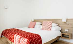 Dobbeltværelse med rødt sengetøj og to puder, væglamper og et natbord. (AI-genereret tekst)