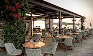 Udendørs serveringsområde med borde og stole og udsigt over havet. (AI-genereret tekst)