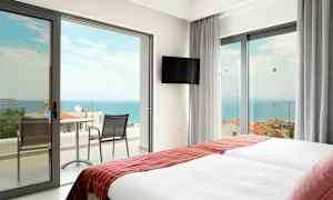 Hotelværelse med to senge og døre til balkon mod havet. (AI-genereret tekst)