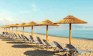 En række solsenge og parasoller af halm på en sandstrand ved havet. (AI-genereret tekst)