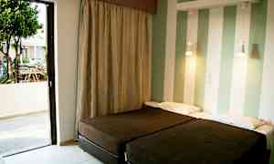 To enkeltsenge i et rum med stribede vægge og en åben balkon dør, der fører til en terrasse. (AI-genereret tekst)